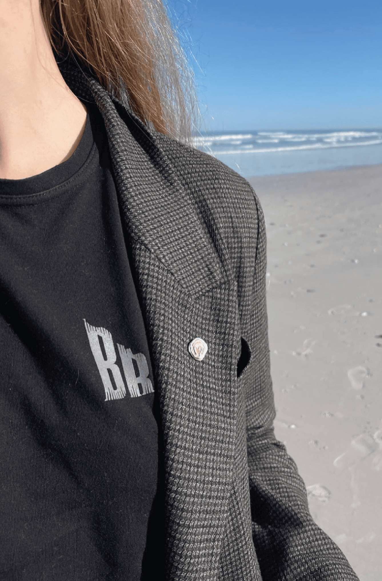 Woman on beach wearing a black t-shirt styled with tailored jacket and silver pin
