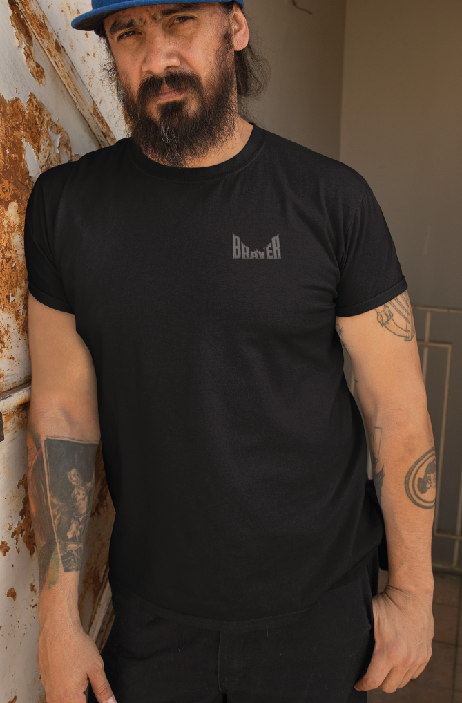 Man with beard and tattoos wearing a black t-shirt with small pocket print saying BRAVER