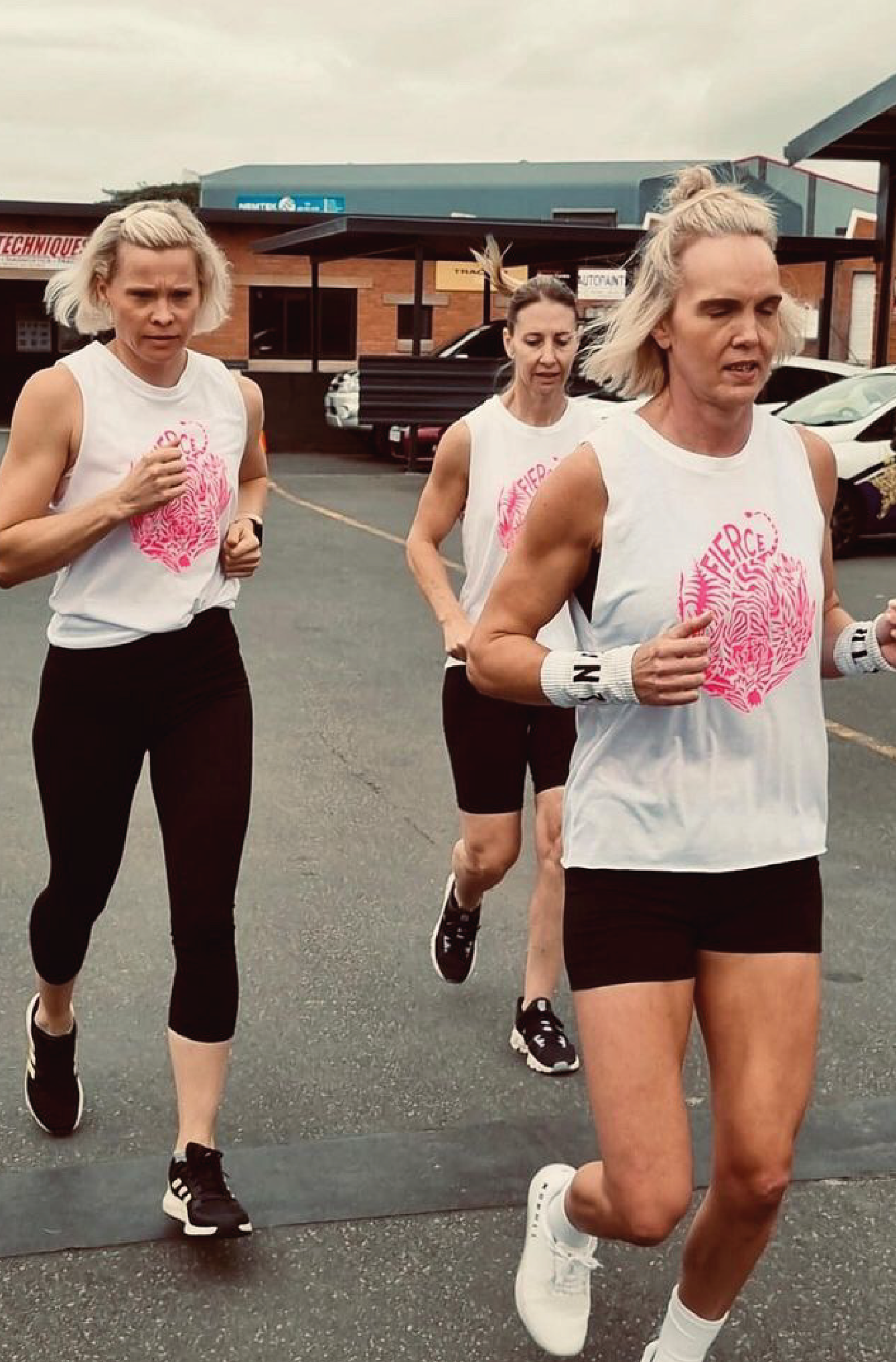 three women running while wearing white tank tops with a neon pink tiger print on the chest