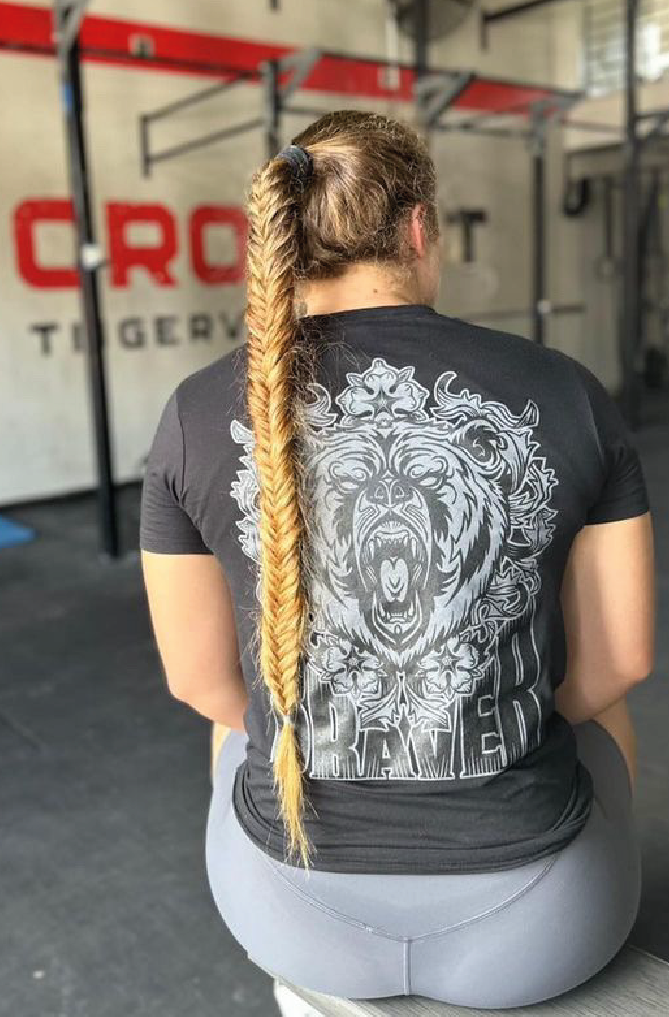 Women pictured from the back with long hear wearing a black t-shirt  and a large grey and black print of a bear face and the word braver