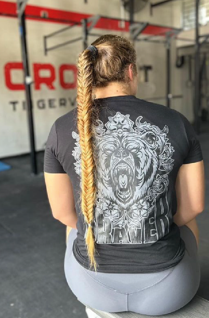 Women pictured from the back with long hear wearing a black t-shirt  and a large grey and black print of a bear face and the word braver