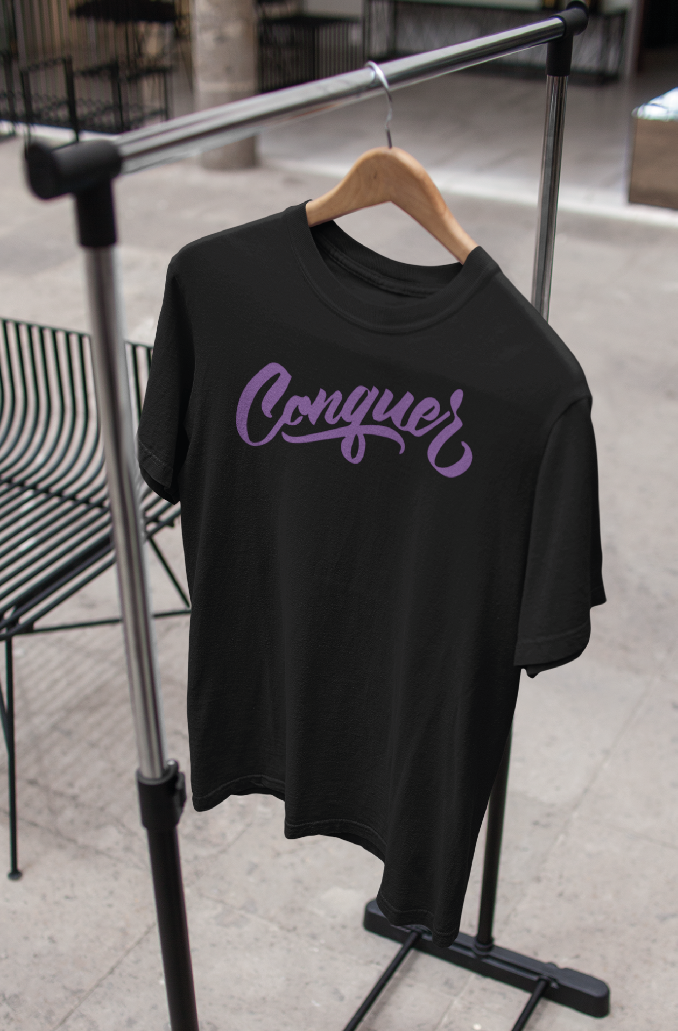Black unisex t-shirt on hanger with the word Conquer printed on the chest in lilac