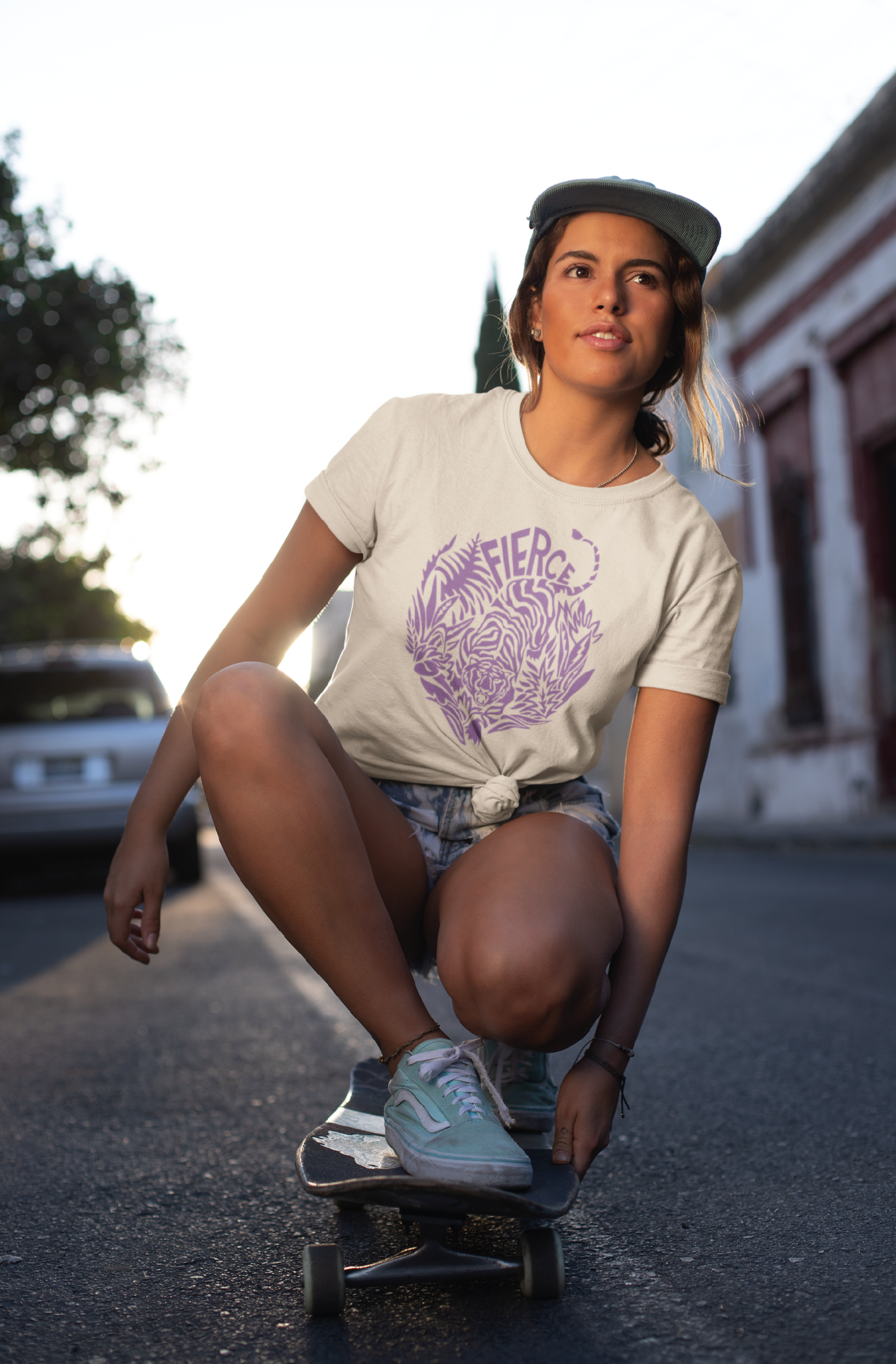 Woman on a skate board wears a sandstone coloured unisex t-shirt with a tiger printed on the front in colour lilac.